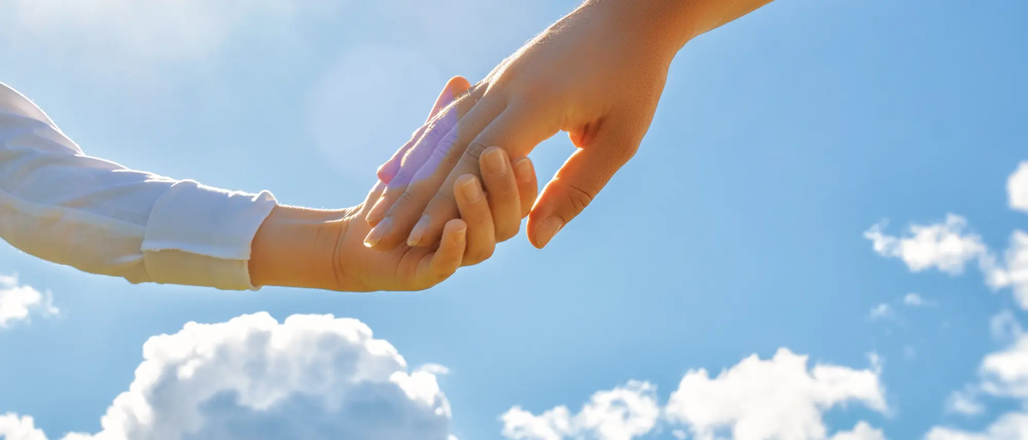 Hands of adult and child on blue sky background