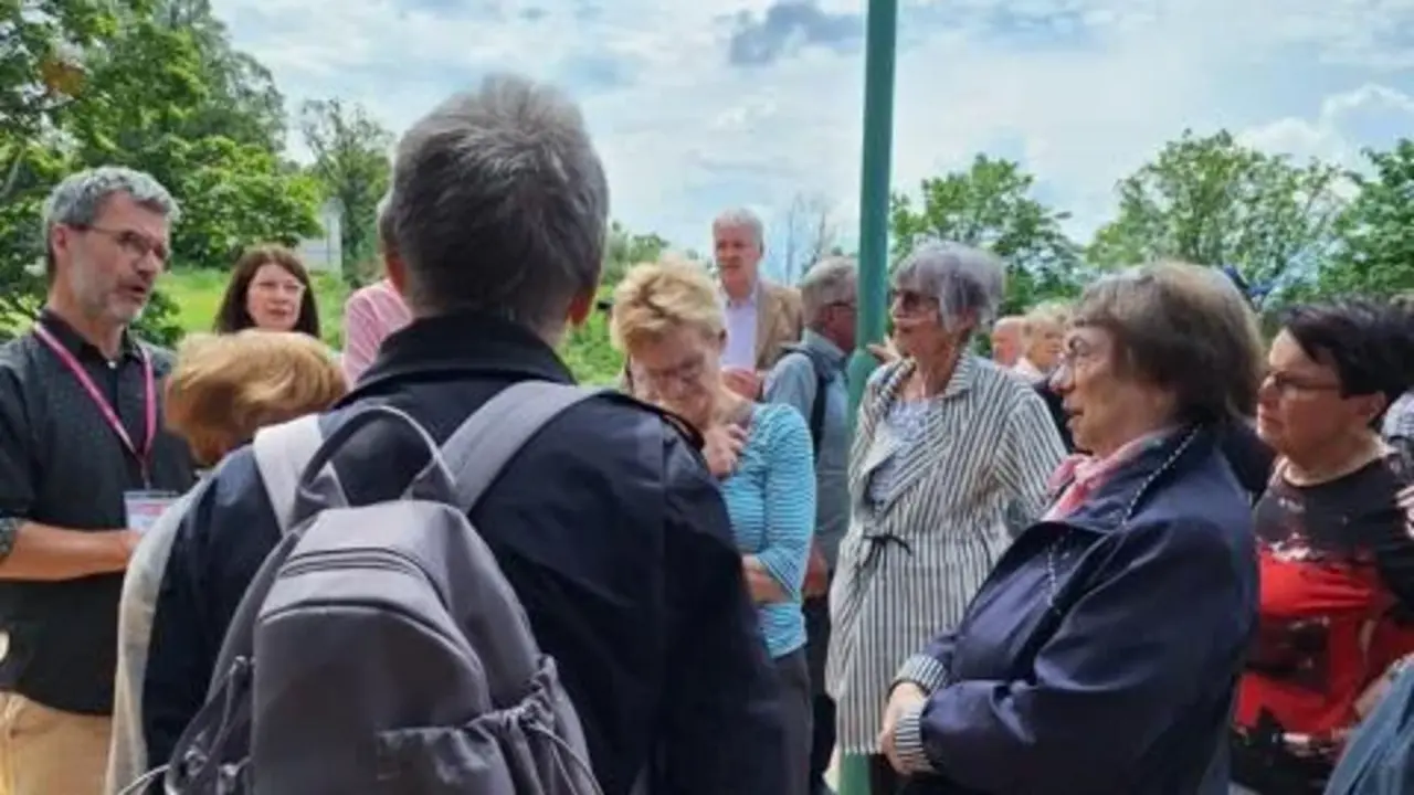 Eine Gruppe von Menschen steht draußen auf einer Terrasse unter bewölktem Himmel, im Gespräch vertieft.