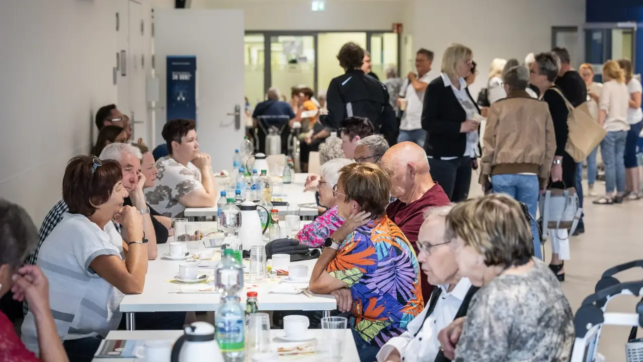 Menschen sitzen in einem Raum an Tischen und unterhalten sich