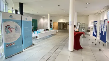 Eine Ausstellungshalle mit Informationsständen und Postern zum Thema pulmonale Hypertonie. Im Vordergrund sind zwei große Banner mit Illustrationen des menschlichen Herzens sichtbar.