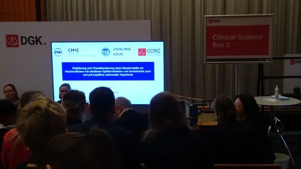 Eine Präsentation bei einer medizinischen Konferenz. Auf dem Bildschirm ist der Titel eines Forschungsprojekts der Uniklinik Köln und anderer medizinischer Institute zu sehen.